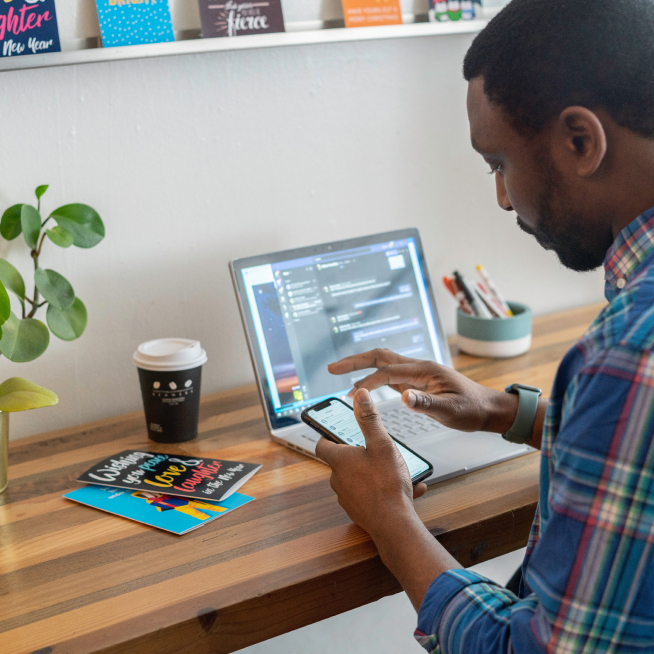 Person working on computer at desk with smart phone.